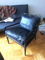 Front three-quarter view of lounge chair showing ebonized wood frame, slatted back, and black leather cushions