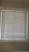 Closed white faux wood blinds installed within a window frame, showing 2-inch slats horizontally arranged and controlled by a side chain.