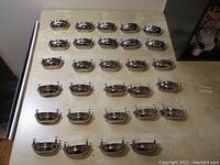 29 chrome metal cup cabinet pulls laid out on a flat surface, showing front side with visible screws.
