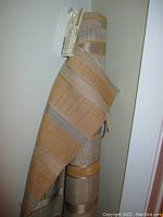 Rolled upholstery fabric showing tan and grey striped woven pattern.