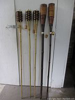 Five bamboo garden torch holders displayed against a white wall showing the full length of each torch, tallest measuring approximately 59 inches.