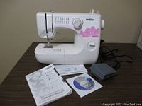 Full frontal view of sewing machine on tabletop with manual, CD-ROM, and foot pedal