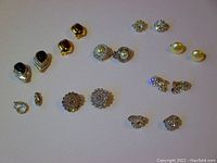 Photo showing nine pairs of clip-on earrings arranged on white background, featuring various designs including faux pearls, black stones, and rhinestones, highlighting the vintage style and condition.