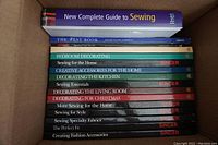 Top view of boxed collection of sewing and home decorating books. Books are neatly stacked with visible titles showing various sewing and decorating topics.