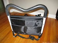 Front view showing white metal frame with curved padded black foam handle and black fabric pocket with adjustable straps