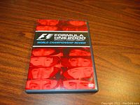 Closed DVD case showing front cover with red tinted images of F1 drivers and title.