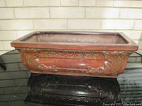 Front angled view of glazed ornamental planter showing reddish-brown finish and decorative embossing.