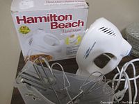 Hamilton Beach hand mixer with box and metal beater attachments displayed on a table.