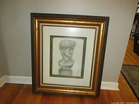 Front view of heavy wooden frame containing framed pencil sketch of classical statue bust, showing full frame and wall background.