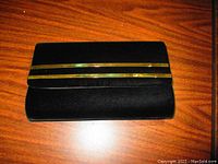 Front view of a black velvet evening clutch with two parallel gold bars on the flap resting on a wooden surface.