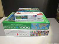 Stack of three jigsaw puzzle boxes showing titles and piece counts