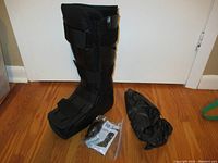 Full view of the black LDK2 AirWalker tall medium boot with straps, black protective cover, and accessories on wooden floor.