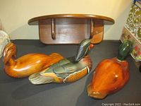 Photo showing three carved wooden duck decoys in varied finishes and colors positioned in front of the wooden shelf to display the decoys and give scale.