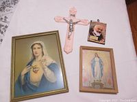 Four framed religious prints and one pink crucifix on table