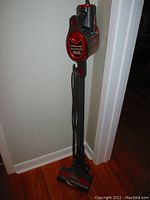 Front view of Rocket bagless standup vacuum cleaner in gray and red with power cord wrapped on handle, resting upright.