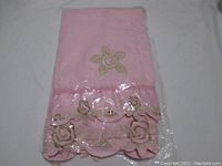 Stacked view of the larger pink towel showing floral embroidery with satin trim in packaging