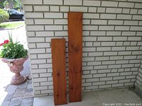 Two wooden pine shelves leaning against a white brick wall outdoors, showing full length of each shelf to display dimensions and finish.