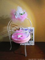 Single white metal plate stand holding pink disposable plates stacked and topped with a pink and white tulle pom decoration with flowers.