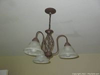 Chandelier hanging mounted on ceiling, showing structure with three frosted glass shades and dark copper metal finish.