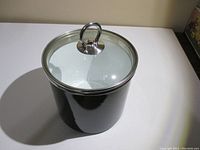 Side angle view of black enamel canister with stainless steel rim and glass lid with loop handle.
