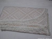 Folded bedspread showing white side with orange gold pattern and fringe detail.
