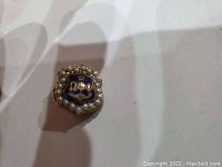 Front view of the gold fraternity pin with blue enamel and pearl border showing Greek letters Phi Omega Psi.