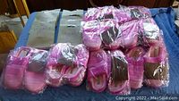 Photo showing 16 pairs of pink William & Kate fleece house slippers, size 36-37, individually wrapped in plastic, arranged on a blue surface along with 7 packages of Legacy Legwear pantyhose in black and beige sizes.