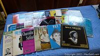 Overview of 23 vintage vinyl records arranged on a blue surface. Covers include diverse artwork and artists.