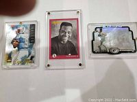 Three sports trading cards in clear protective cases showing front images including Steve McNair, Frank Thomas, and Mark McGwire.