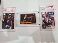 Three sports cards laid out in a row: John Elway graded card (left), Cal Ripken card in plastic holder (center), Terrell Davis graded card (right).