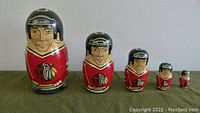 Front view of 5 Chicago Blackhawks nesting dolls arranged largest to smallest on a green surface.