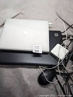 Apple iBook laptop closed on top of HP laptop with charger and cables visible