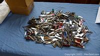 Overall view of a large pile of assorted nail clippers, keychains, and pocket multi-tools in various styles and materials, laid on a blue surface.