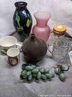Collection of various glass and ceramic vessels and decorative grapes arranged together on a white background.