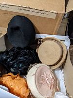 Photo showing various women's hats including black felt, feathered, and straw hats with ribbons packed in a box.
