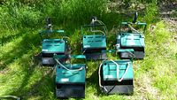 Five teal and black rectangular spotlight lighting units arranged on grass with attached power cords and carrying handles visible.