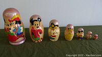 Full view of all 7 nesting dolls lined up from largest to smallest, hand-painted with Disney characters including Mickey Mouse, Minnie Mouse, Pluto, and Goofy in colorful attire.