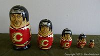 Five hand-painted wooden nesting dolls representing NHL Calgary Flames players arranged in descending size from left to right against a gray background.