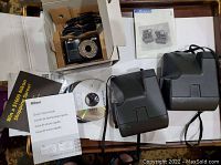 Photo showing Nikon Coolpix L22 camera box, manuals, software CD, battery charger, and cables laid out on a table.