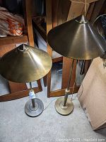 Two heavy brass table lamps placed side by side, showing their overall shape and size with cone-shaped shades and round bases.