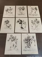 Eight unframed black and white NFL player art prints laid out on floor, showing full set.