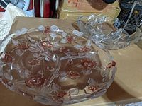 Two Mikasa Bella Rose glass serving trays, one round with pink rose accents and one square with floral leaf design, displayed on cardboard box background.