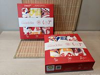 Two boxed aden+anais Product(RED) organic cotton swaddle sets arranged side by side on a woven mat. Boxes are red with white labeling and colorful swaddle patterns visible.
