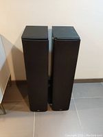 Front view of two Bowers & Wilkins black floor standing speakers with fabric grills on, showing full height and shape.