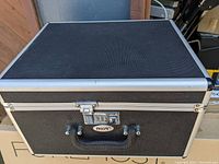 Closed black carrying case with metal reinforcements and latch, labeled INYA.