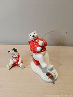 Front view of two Coca-Cola themed polar bear ceramic figurines on a surface, one fishing polar bear and one smaller seated bear.