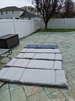 Five pool lounger cushions laid out on outdoor concrete, showing four solid gray cushions and one blue striped cushion.