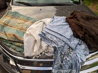 Eight curtains laid out and folded on a car hood showing various colors and patterns: brown solid, blue solid with tassels, patterned multicolor with stripes, and white textured with tassels.