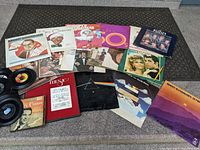 Wide shot of collection on a textured floor showing album covers, framed sheet music, and loose records.