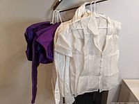 Set of 8 garments hanging on hanger including 4 purple boleros and 4 white blouses showing fabric and style